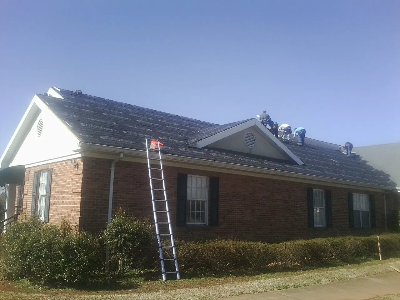 Crew tearing shingles off a brick ranch roof with a ladder set — Emergency Roof Repair work by our crew in Round Lake