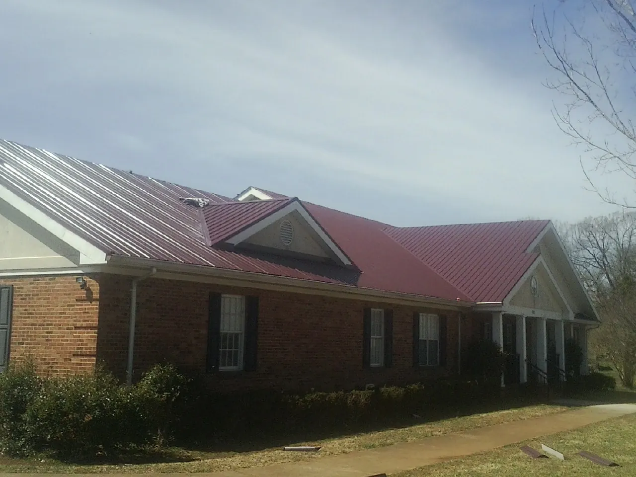 Red metal roof with gabled entries on a long brick building, from a Hail Damage Roof Repair job in Round Lake