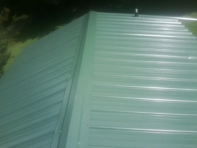 New green metal panels meeting at the ridge of a roof — Flat Roof Repair work by our crew in Round Lake